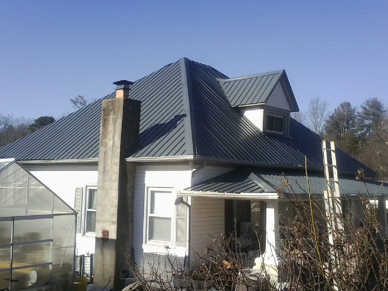 Dark blue standing seam metal roof on a white farmhouse with dormer — Slate & Tile Roof Repair by Roofing Brothers in Clinton Township