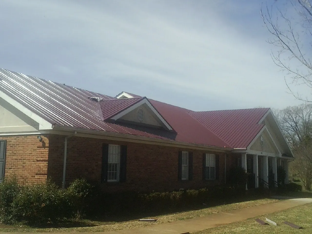 Red metal roof with gabled entries on a long brick building, from a Hail Damage Roof Repair job in Clinton Township