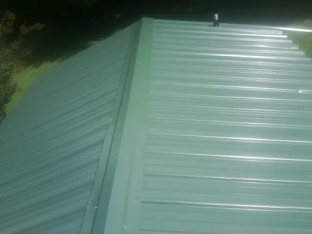 New green metal panels meeting at the ridge of a roof — Flat Roof Repair work by our crew in Clinton Township