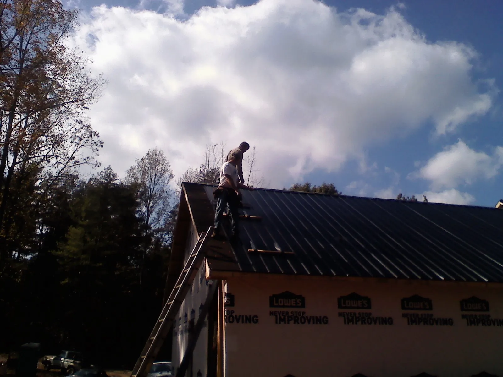 Roofer fastening dark metal panels high against a cloudy sky, from a Roof Inspection job in Clinton Township