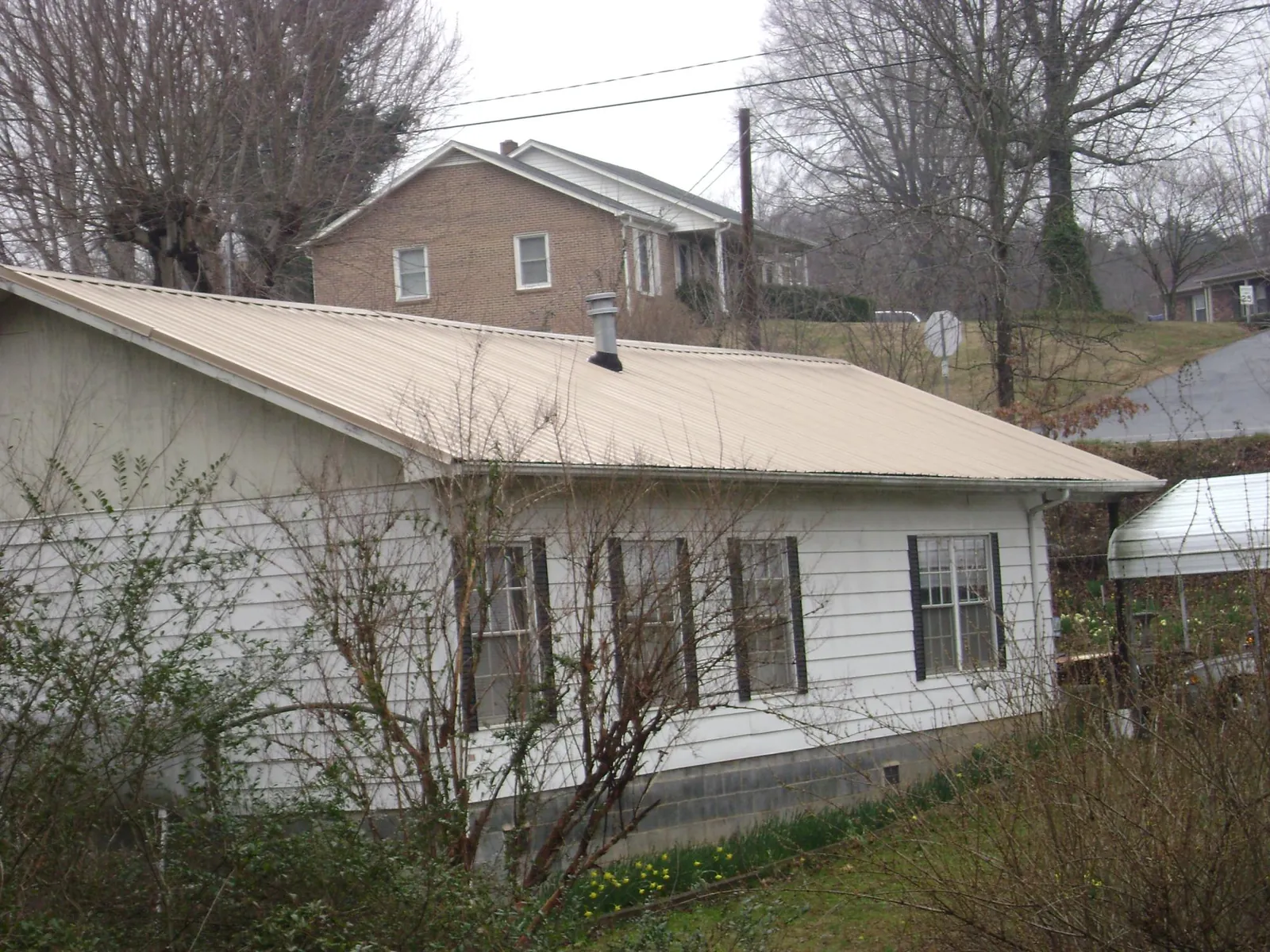 Tan metal roof on a white sided house set into a hillside — Commercial Roofing by Roofing Brothers in Clinton Township